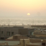 Sunset Seaview From Luxurious Apartment In Dha Phase 5, With Sea Horizon, Beach Waves, Promenade, People, Cars, And Modern Bu