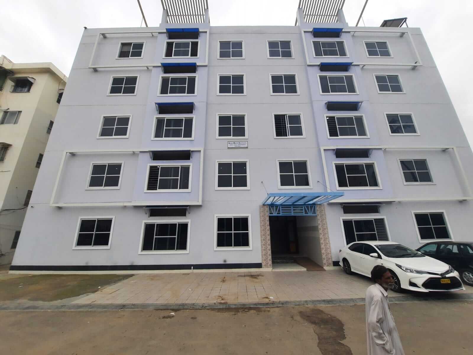 Dunes Marvel Clifton Modern 3 Bedroom Apartment For Sale In Boat Basin Block 5 Clifton Karachi Modern facade of Dunes Marvel Clifton apartment building with white exterior, blue balconies, multiple floors, entrance canop