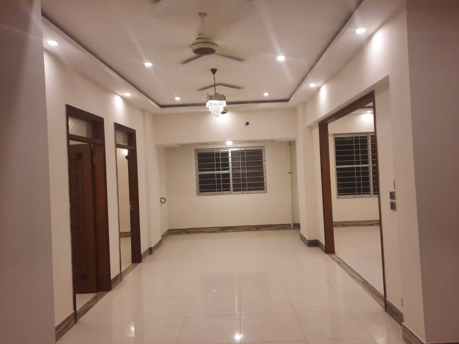 Dunes Marvel Clifton 3-Bedroom Flat for Sale in Clifton Block 5 Karachi (11) Spacious empty living area in Dunes Marvel Clifton 3-bedroom flat, Clifton Block 5 Karachi with white tiles and wooden doors