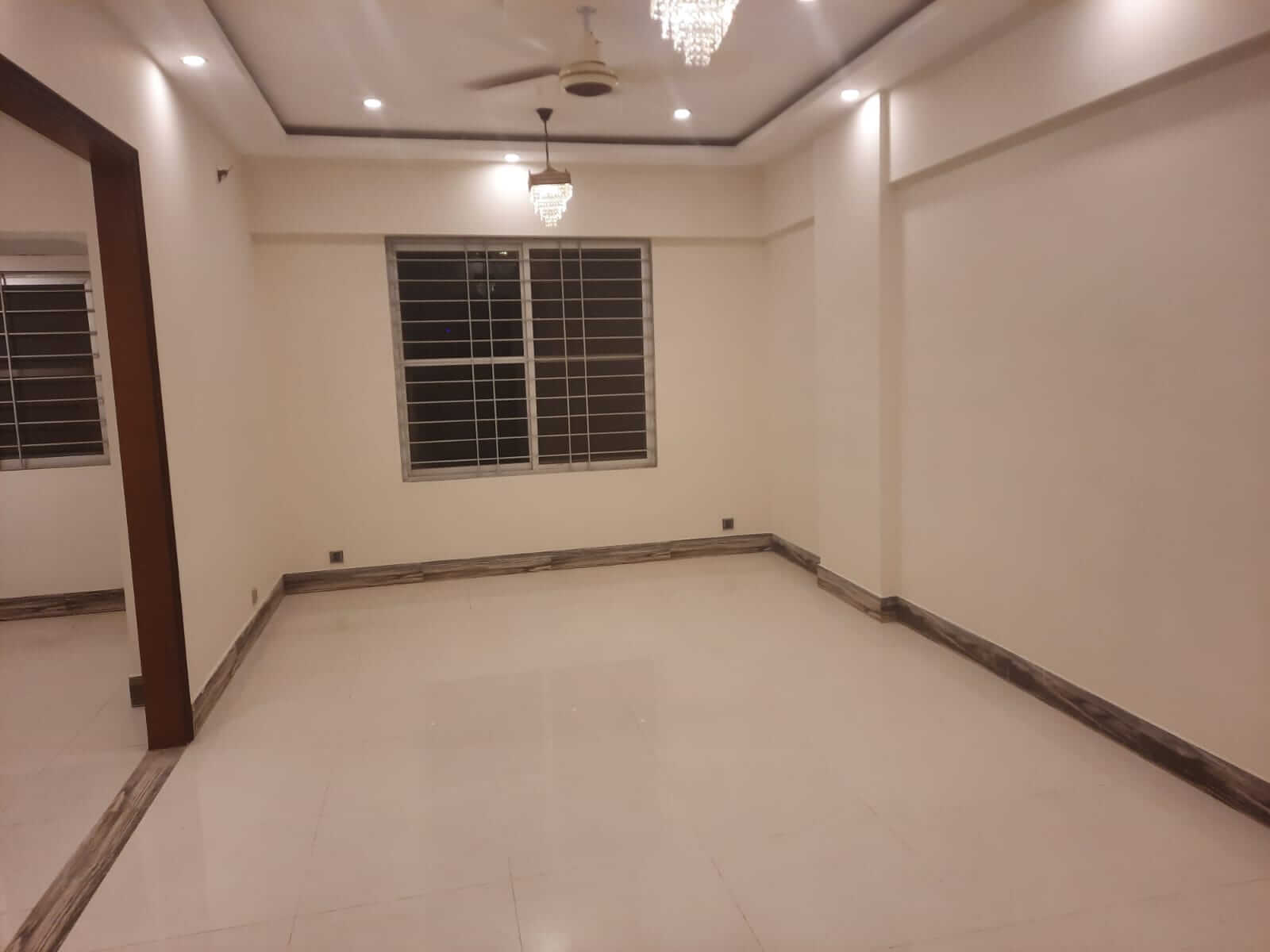 Dunes Marvel Clifton 3-Bedroom Flat for Sale in Clifton Block 5 Karachi (13) Spacious empty room in Dunes Marvel Clifton flat with white marble floors, large barred window and ceiling chandeliers in Cli