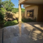 Luxury Bungalow Exterior In Dha Phase 6 With Beige Tiled Patio, Green Lawn, Rock Garden, Pillars, And Arched Windows