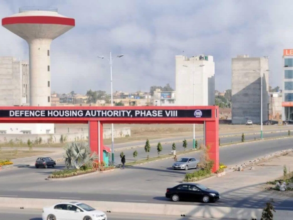 Dha Phase Viii Entrance Gate In Karachi With Red Archway, Water Tower, High-Rises, Palm Trees And Vehicles