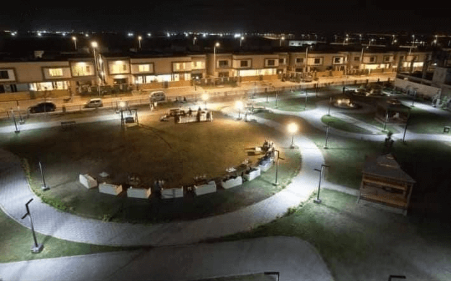 Night aerial view of modern villas surrounding lit central park with paths and seating in Askari 6 Karachi