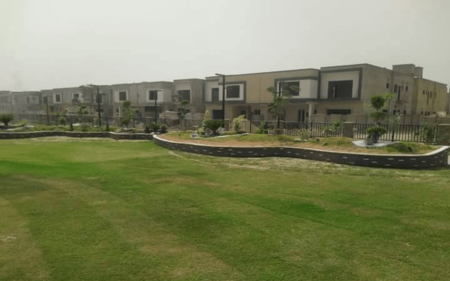 Modern villas in Askari 6 Karachi with beige facades, large windows, balconies, green lawn, palm trees, shrubs, and black met