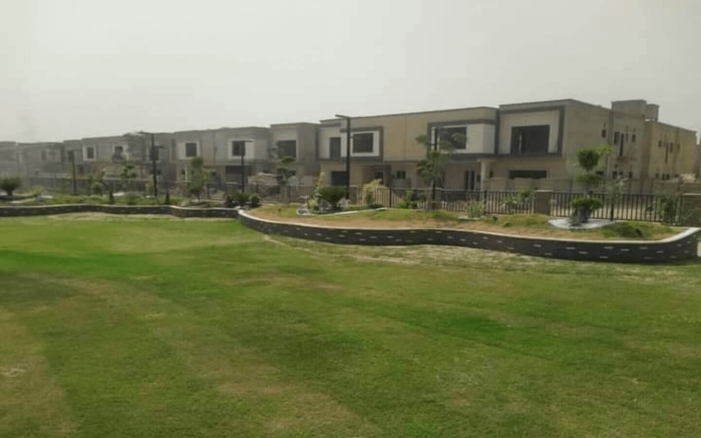 Askari Villas Karachi 270 Sq Yd Luxury by MaxX Capitals (10) Row of modern Askari Villas with beige facades, large windows, balconies, and landscaped green lawns at Askari VI, Karachi