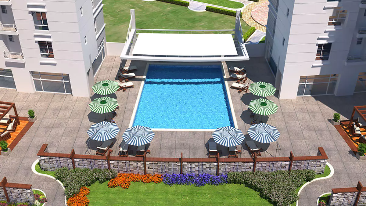 Luxury Living 4 Bedrooms Flat for Rent In COM3 Tower Clifton Block 6 Karachi (6) Aerial view of rectangular blue swimming pool with loungers, colorful umbrellas, deck, gardens and white towers in Com3 Tower