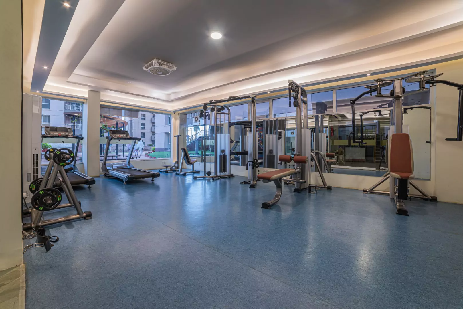 Luxury Flats & Penthouses For Sale in Lakhani Presidency (8) Spacious gym at Lakhani Presidency in Karachi with treadmills, weight machines, benches, blue flooring, and large windows