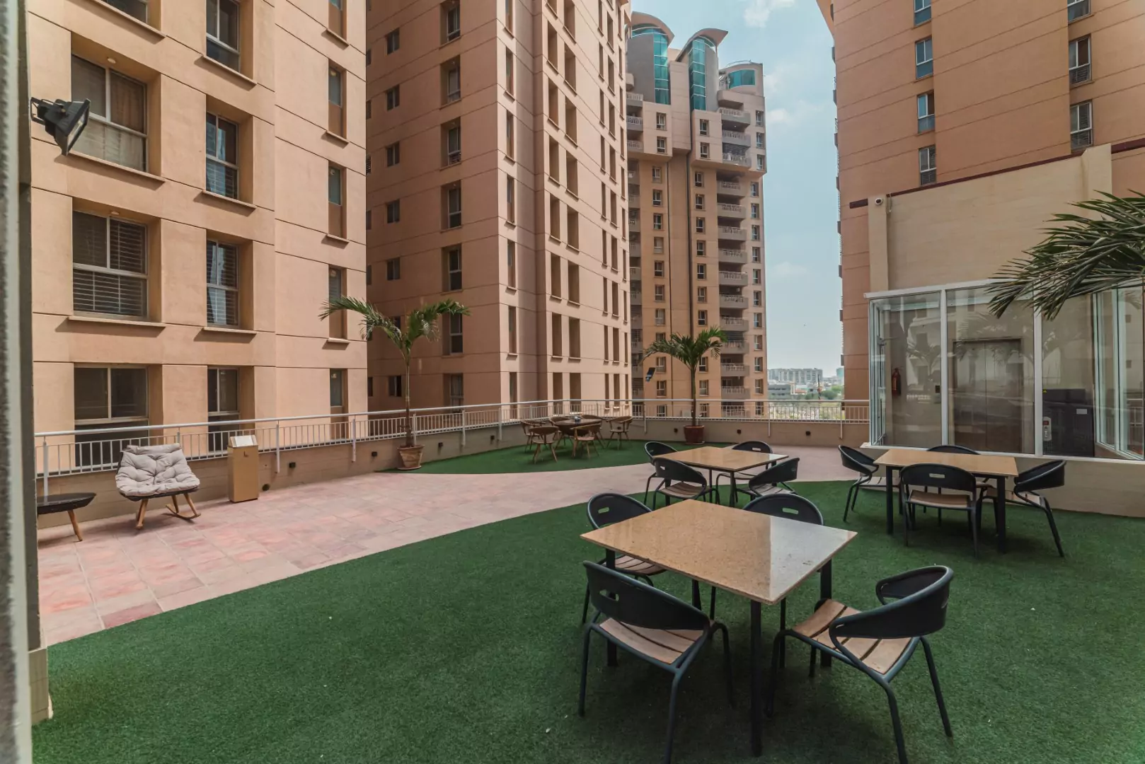 Luxury Flats & Penthouses For Sale in Lakhani Presidency (9) Rooftop terrace at Lakhani Presidency in Karachi with artificial turf, lounge seating, tables, chairs, potted palms, and surr