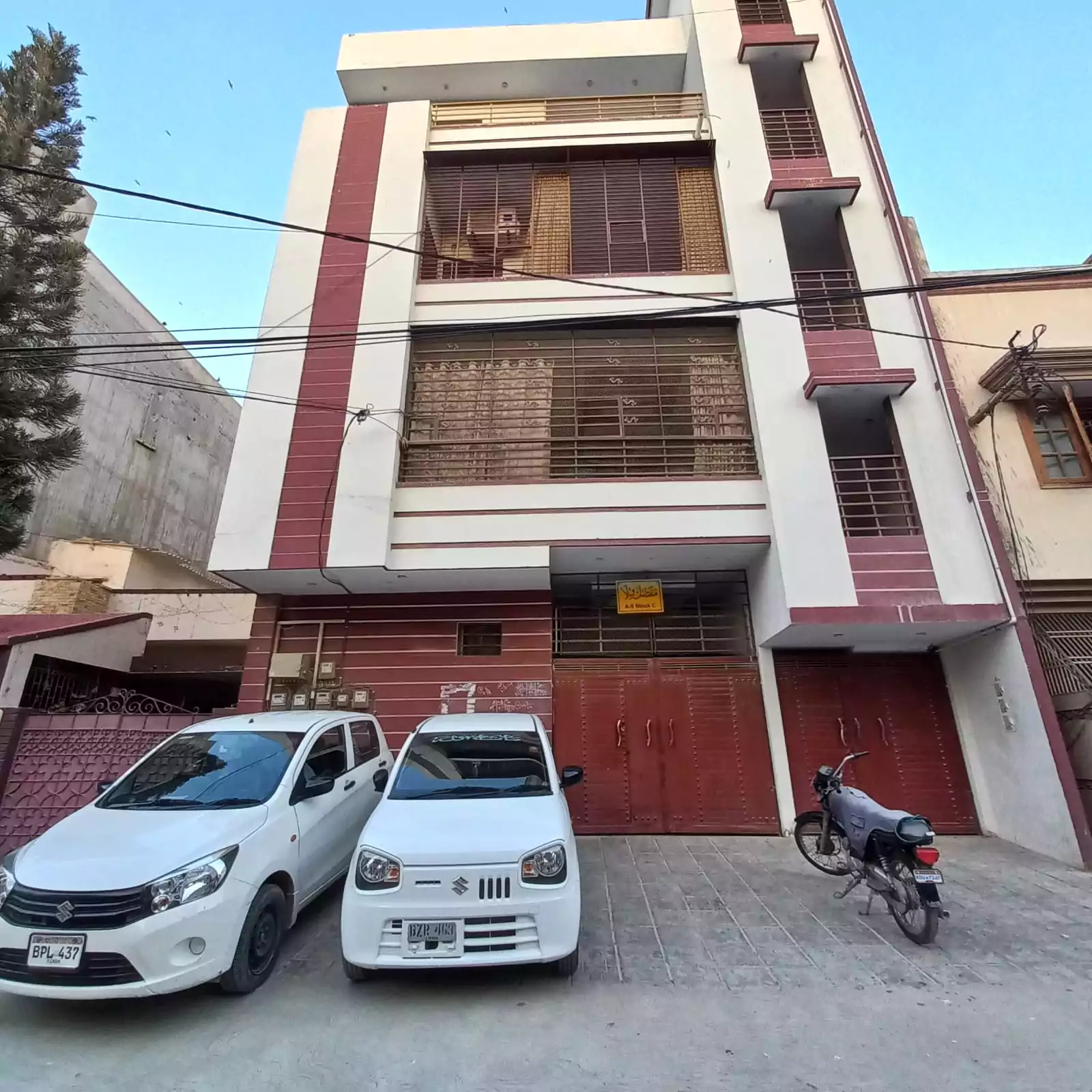 Ground floor portion for sale in North Nazimabad Block C, modern white house with maroon accents, gated driveway, two parked 