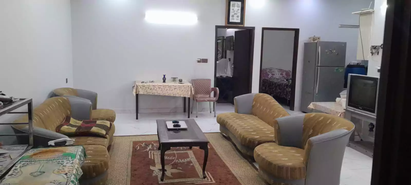 Prime Ground Floor Portion for Sale in North Nazimabad Block C Karachi (2) Spacious living room in North Nazimabad Block C ground floor portion with beige sofas, dining table, TV, fridge, wardrobe