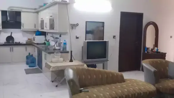 Ground floor portion kitchen-living area in North Nazimabad Block C with white cabinets, fridge, sink, brown sofas, TV and ti