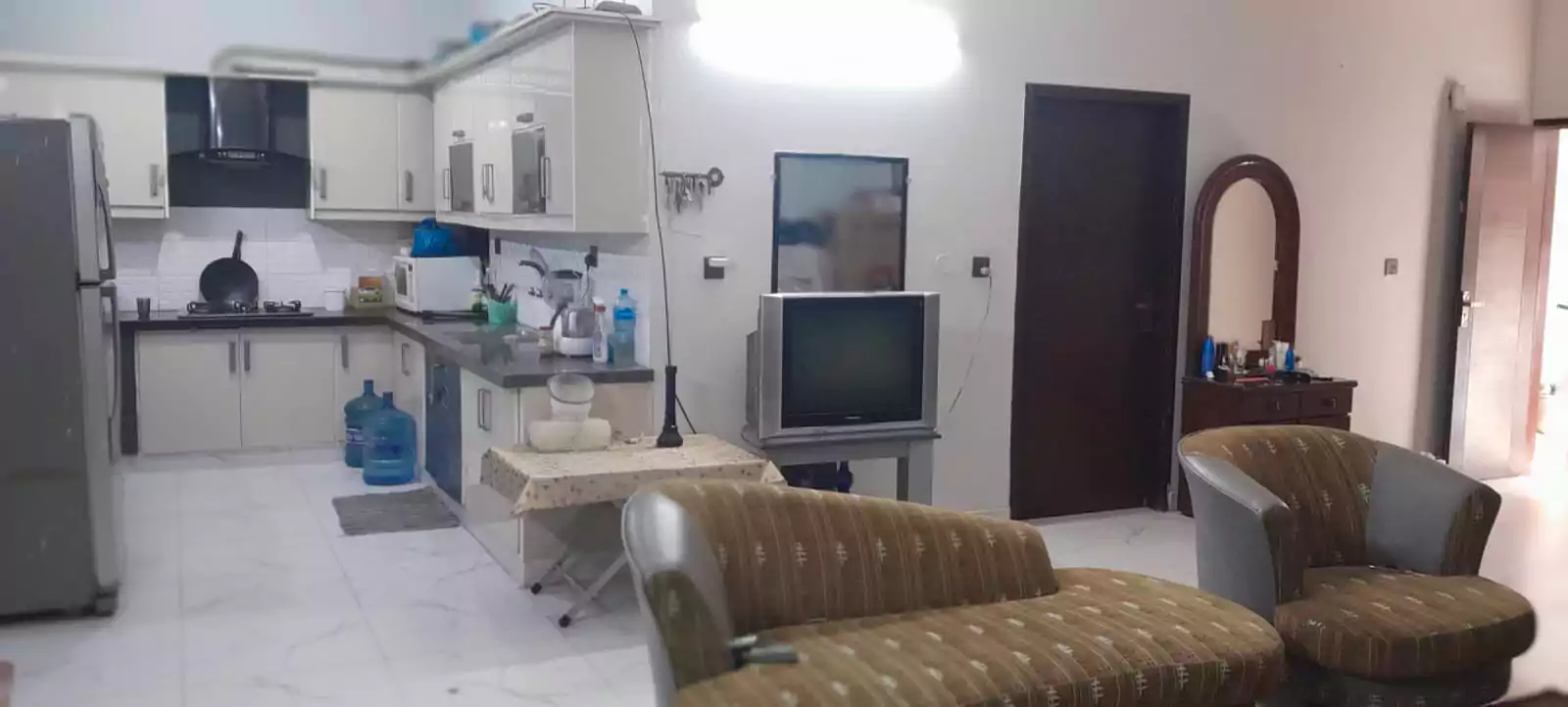 Prime Ground Floor Portion for Sale in North Nazimabad Block C Karachi (3) Ground floor portion kitchen-living area in North Nazimabad Block C with white cabinets, fridge, sink, brown sofas, TV and ti