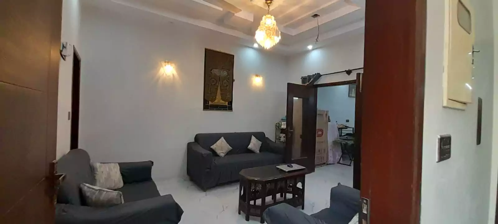 Prime Ground Floor Portion for Sale in North Nazimabad Block C Karachi (5) Living room in ground floor portion for sale North Nazimabad Block C with gray L-shaped sofa, coffee table, chandelier, wall