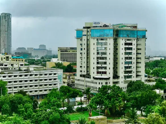 Abeeda Tower Luxury Apartment Building In Civil Lines, Tall White Facade With Blue Accents, Surrounded By Greenery And Urban 