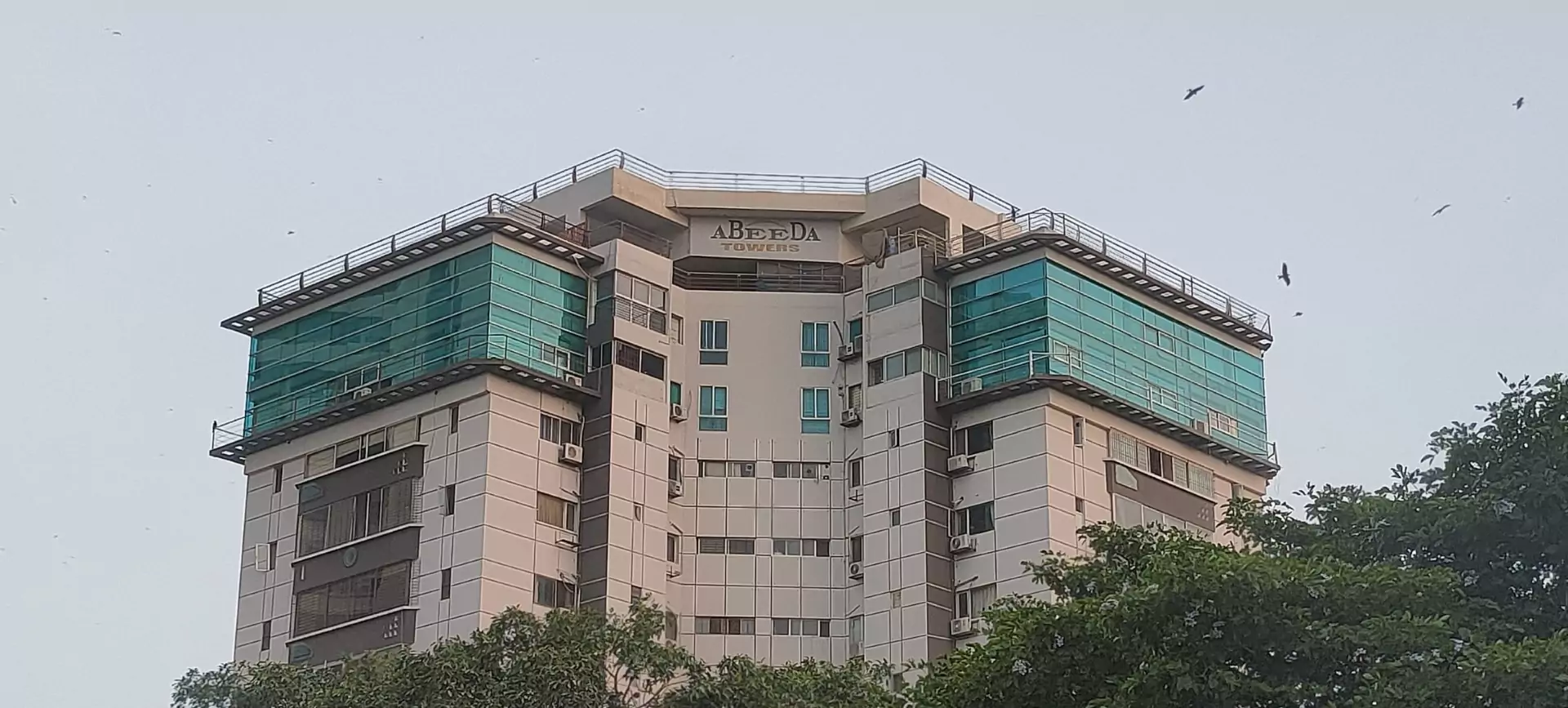Abeeda Tower 4-Bed Luxury Apartment For Sale in Civil Lines, Karachi (3) Abeeda Tower in Civil Lines, high-rise apartment building with white facade, green glass panels, balconies and surrounding tr