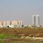 Vacant Commercial Plot In Peninsula Commercial Dha Phase 8 With Foreground Open Land And Background High-Rise Apartment Tower