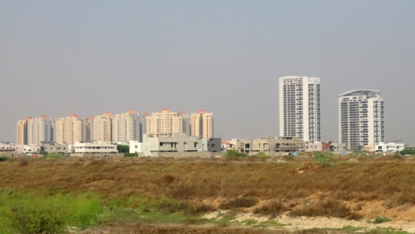 Vacant Commercial Plot In Peninsula Commercial Dha Phase 8 With Foreground Open Land And Background High-Rise Apartment Tower