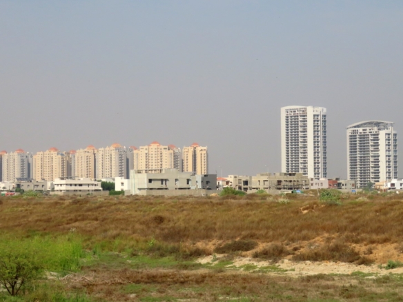 Vacant Commercial Plot In Peninsula Commercial Dha Phase 8 With Foreground Open Land And Background High-Rise Apartment Tower