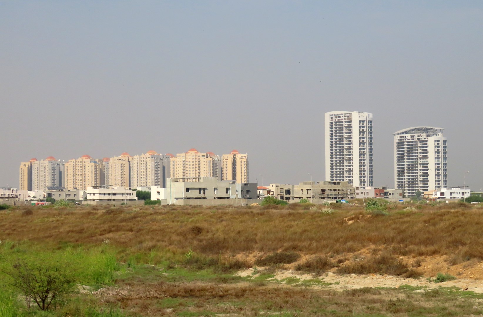 Prime Commercial Plot for Sale in Peninsula Commercial, DHA Phase 8 Karachi (1) Vacant commercial plot in Peninsula Commercial DHA Phase 8 with foreground open land and background high-rise apartment tower