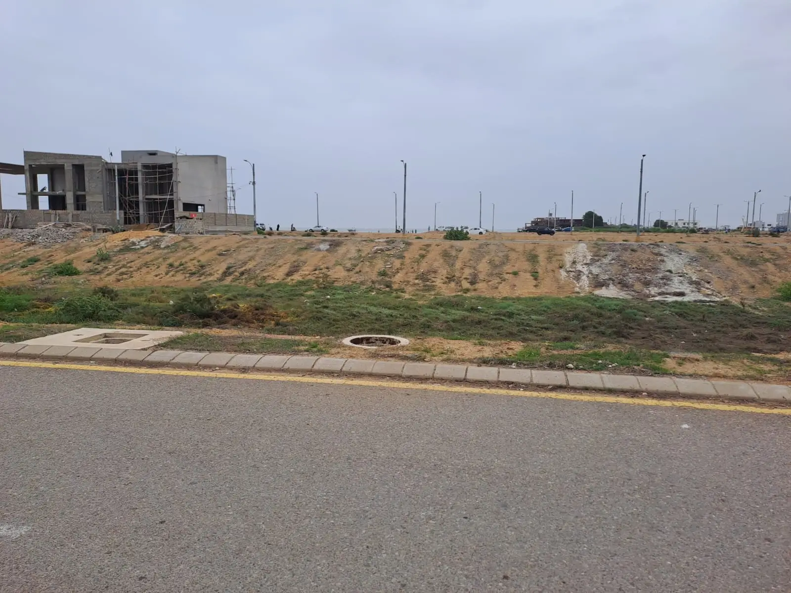Prime Commercial Plot for Sale in Peninsula Commercial, DHA Phase 8 Karachi (2) Commercial plot for sale in Peninsula Commercial DHA Phase 8: vacant land with adjacent under-construction buildings, street