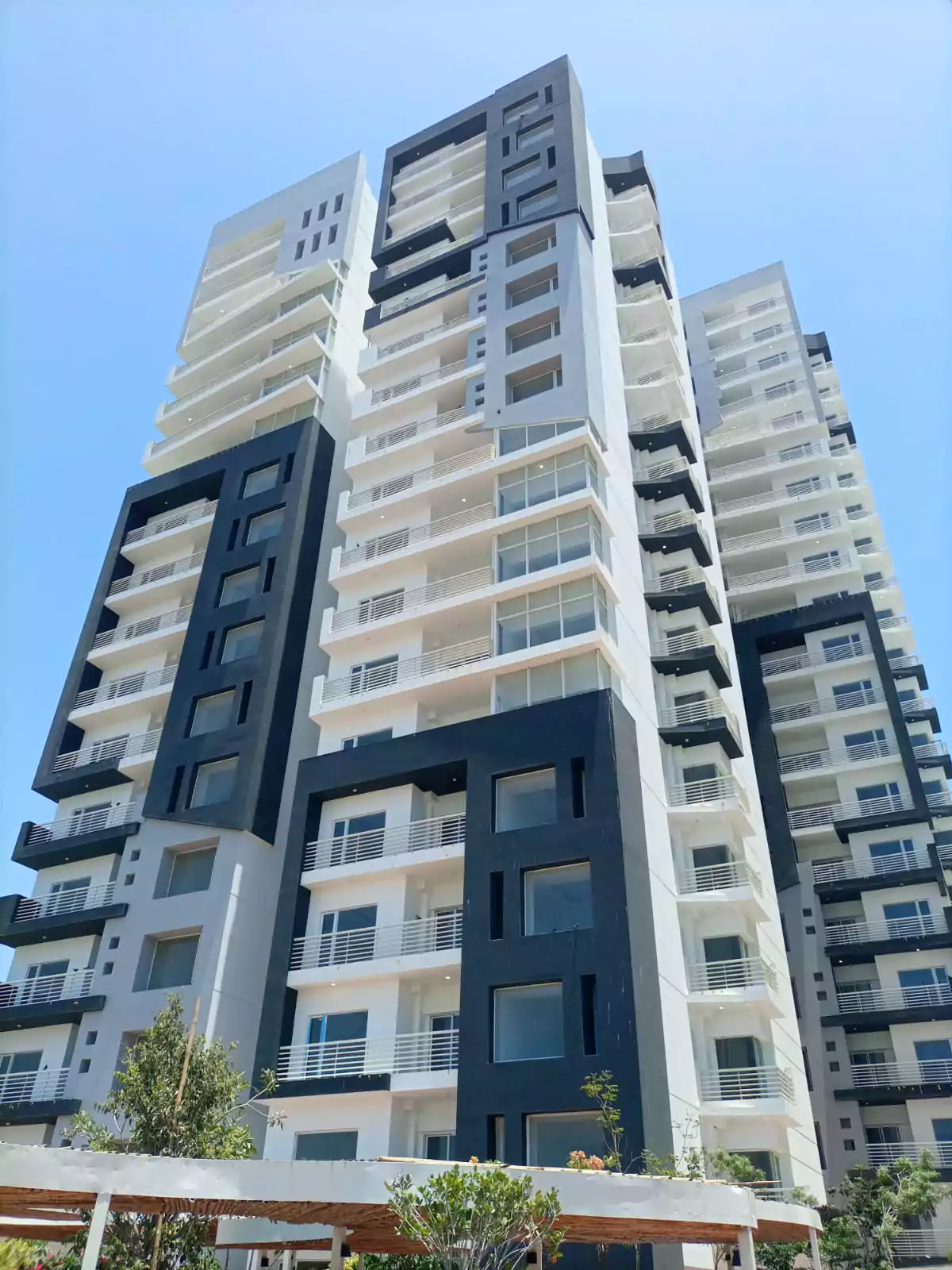 Dynasty Apartments Clifton Luxury 4-Bedroom Flats for Sale in Karachi (10) Modern high-rise facade of Dynasty Apartments Clifton with black and white panels, balconies, large windows, and pool deck