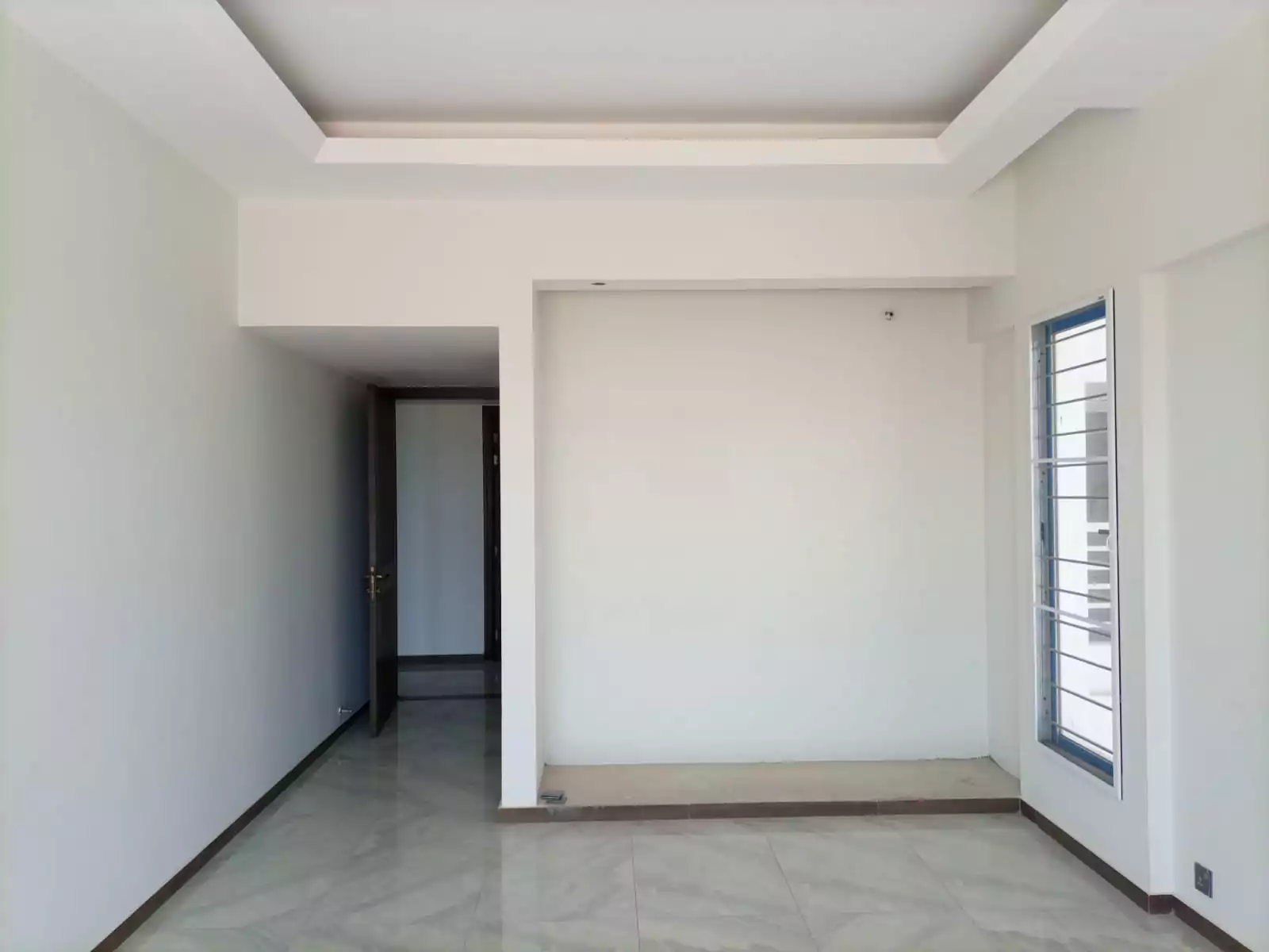 Dynasty Apartments Clifton Luxury 4-Bedroom Flats for Sale in Karachi (4) Spacious empty bedroom in Dynasty Apartments Clifton with white walls, gypsum ceiling, glossy tiled floor, large blue-framed