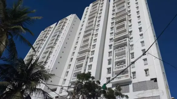 Tall White High-Rise Towers Of Greens One Clifton With Balconies, Palm Trees, And Blue Sky