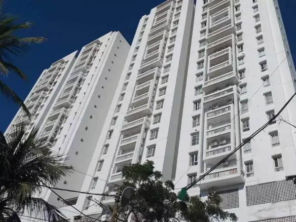 Tall White High-Rise Towers Of Greens One Clifton With Balconies, Palm Trees, And Blue Sky