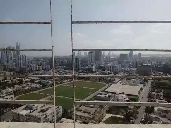 Panoramic city view from Greens One Clifton apartment balcony with high-rises, sports field, and urban skyline