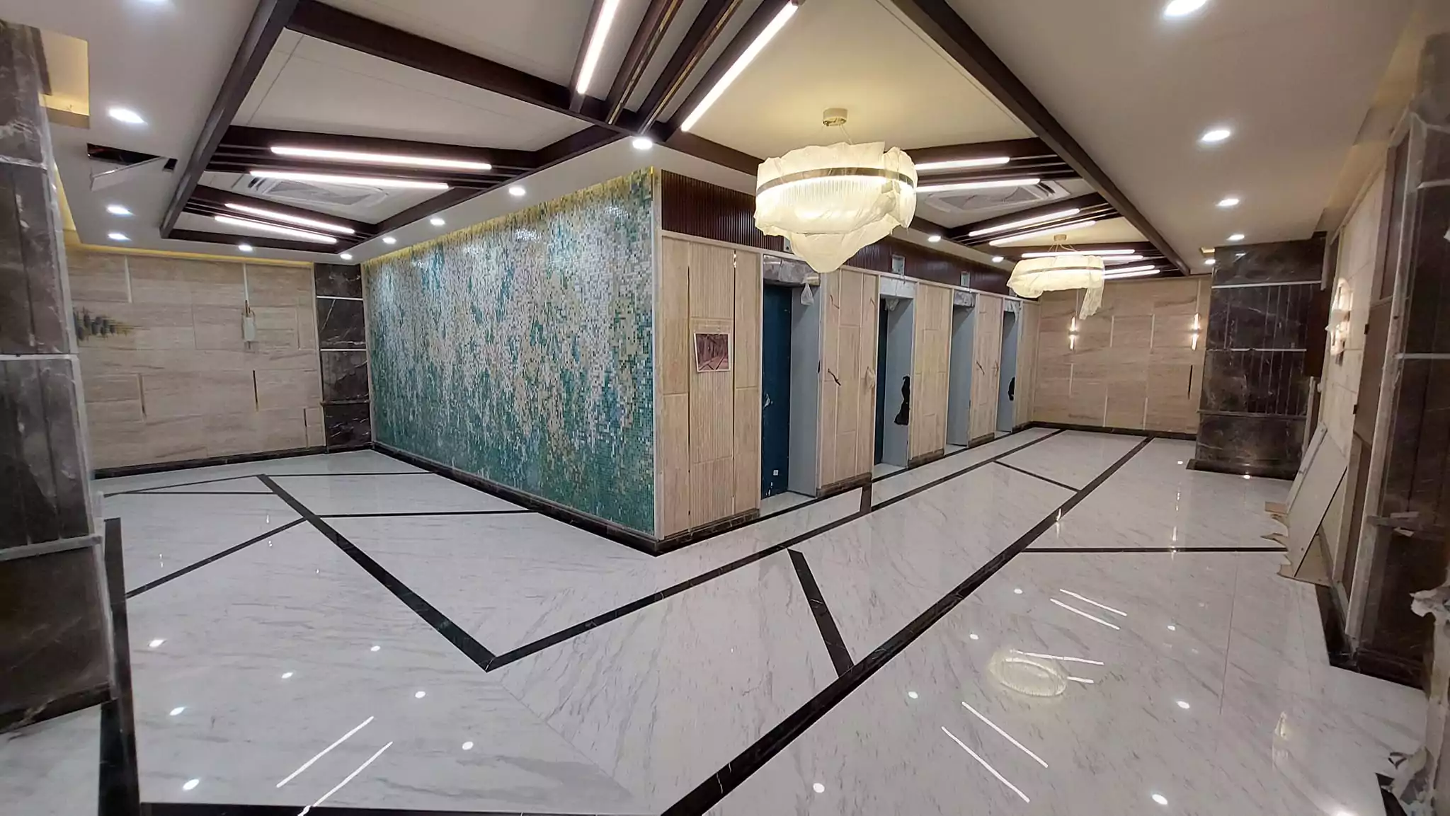 Luxurious 3-Bedroom Apartment for Sale in Green One Clifton Block 8 Karachi (9) Elegant elevator lobby in Greens One Clifton with marble floors, teal mosaic walls, wooden panels, and pendant lights