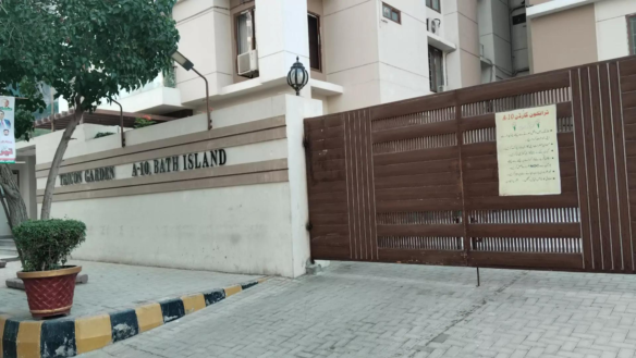 Gated Entrance Of Venus Garden - Bait Island With Beige Walls, Mature Trees, Potted Plants, Metal Slat Gate, And Signage