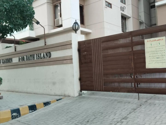 Gated Entrance Of Venus Garden - Bait Island With Beige Walls, Mature Trees, Potted Plants, Metal Slat Gate, And Signage