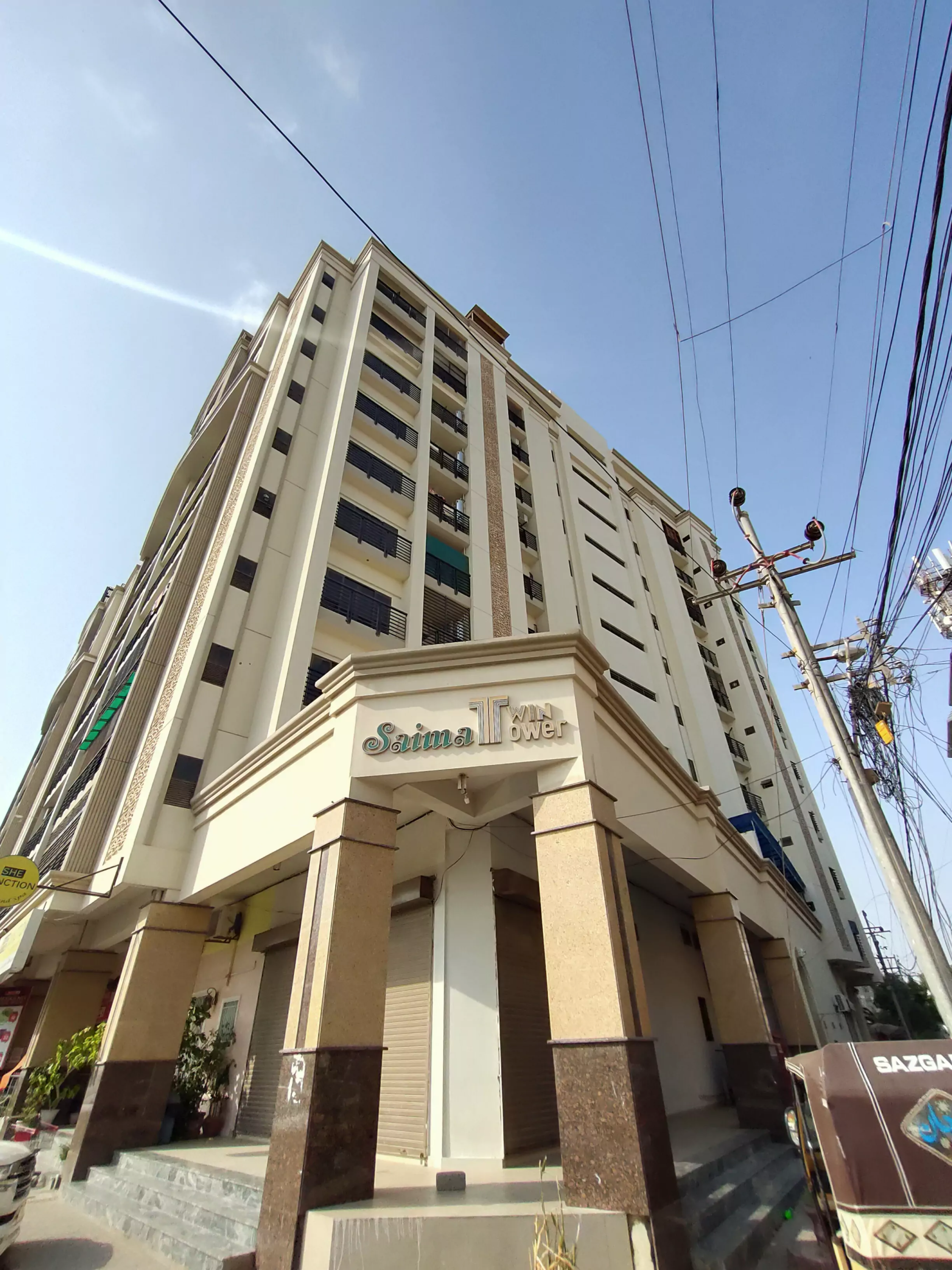 Saima Twin Towers exterior in KDA Scheme 1, multi-story beige building with balconies, pillars at entrance, and signage