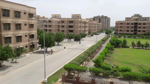 Aerial View Of Multi-Story Beige Apartment Buildings, Central Paved Road, Lush Green Lawns, Trees, And Park In Residential Co