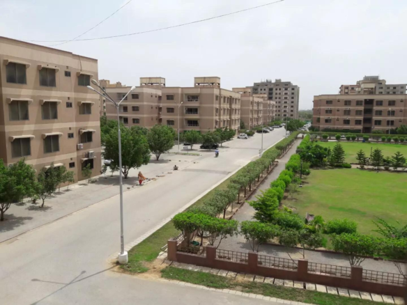 Aerial View Of Multi-Story Beige Apartment Buildings, Central Paved Road, Lush Green Lawns, Trees, And Park In Residential Co
