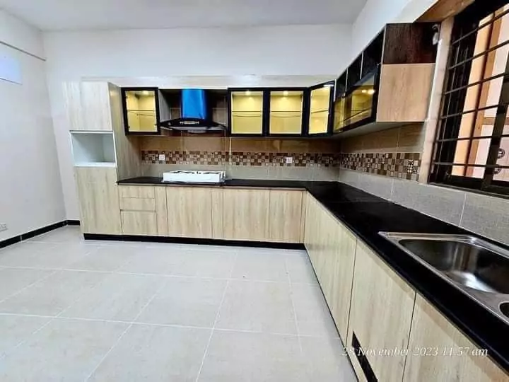 Luxurious 3 Bedroom Flat for Rent in Askari 5, Sector J Malir Cantonment Karachi (7) Modern L-shaped kitchen with light wood cabinets, black countertop, double sink, gas stove, and blue chimney hood in 3-bedroo