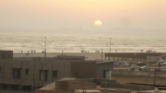 Sunset Seaview From Luxurious Apartment In Dha Phase 5, With Sea Horizon, Beach Waves, Promenade, People, Cars, And Modern Bu