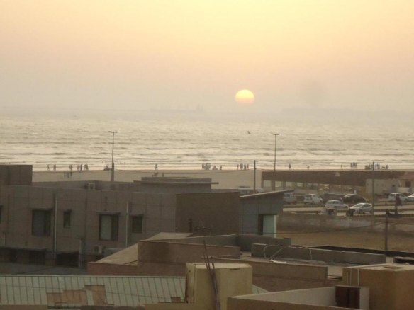 Sunset Seaview From Luxurious Apartment In Dha Phase 5, With Sea Horizon, Beach Waves, Promenade, People, Cars, And Modern Bu