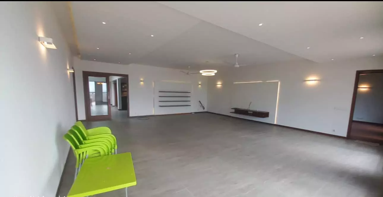 Luxurious 5-Bed Penthouse for Rent in Mall Square Zamzam – DHA Phase 5 Karachi (10) Spacious open-plan living area in 5-bed penthouse for rent in Mall Square DHA, modern white walls, high ceilings, green chair