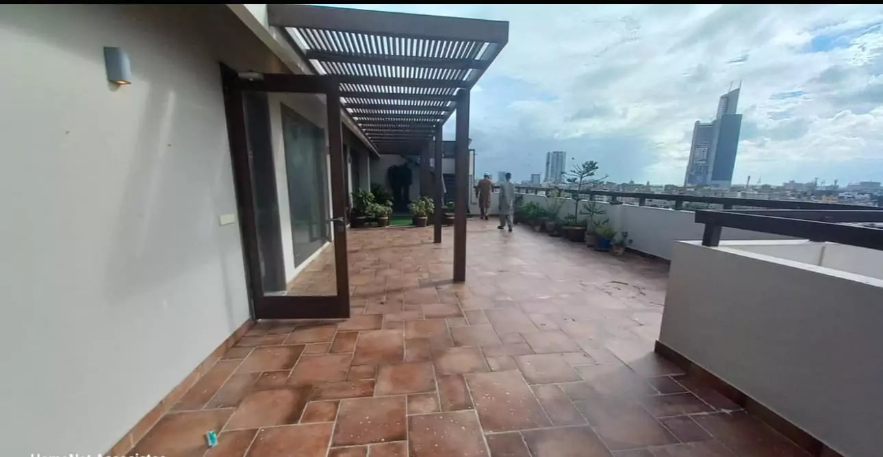 Luxurious 5-Bed Penthouse for Rent in Mall Square Zamzam – DHA Phase 5 Karachi (3) Spacious terrace of 5-bed penthouse for rent in Mall Square DHA with terracotta tiles, pergola, plants, glass doors, and city