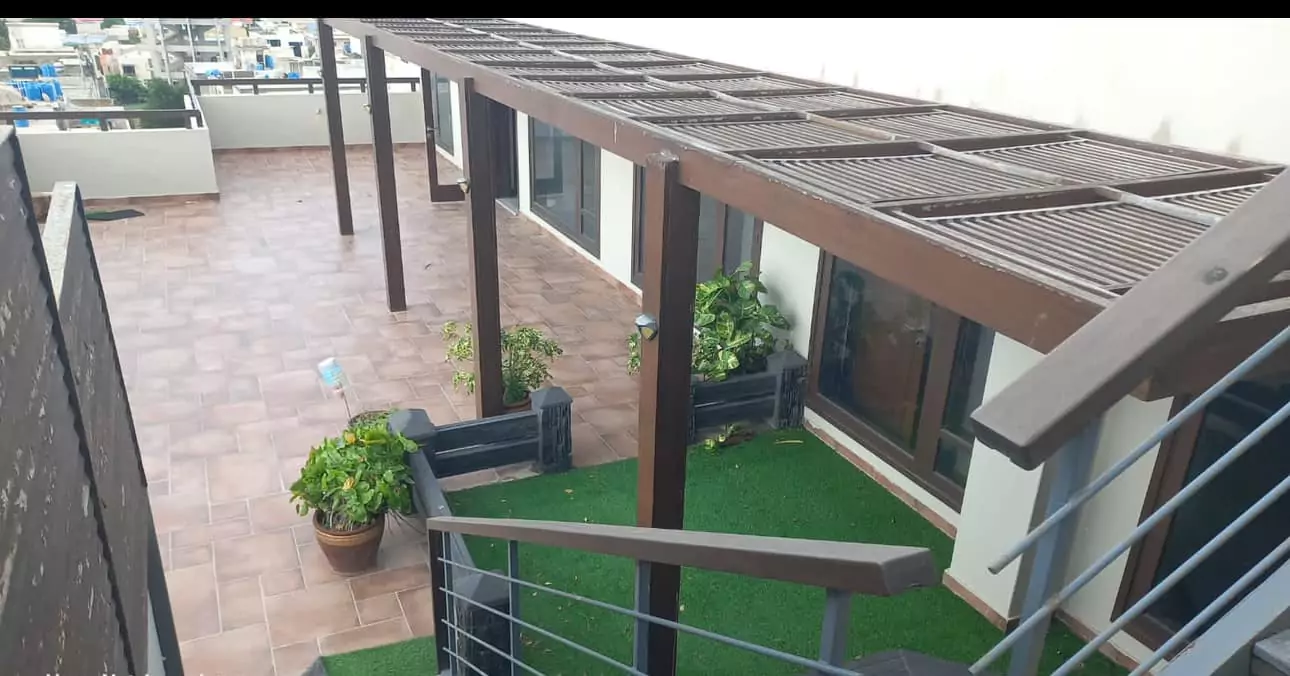 Luxurious 5-Bed Penthouse for Rent in Mall Square Zamzam – DHA Phase 5 Karachi (8) Rooftop terrace of luxurious 5-bed penthouse in Mall Square DHA with wooden pergola, terracotta tiles, potted plants, artific