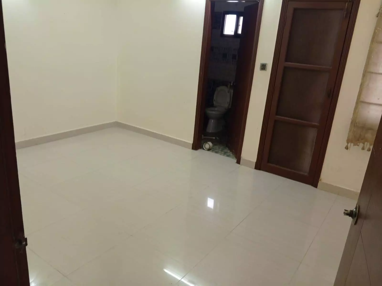 Luxury 3-Bedroom Portion for Rent in PECHS Block 6, Karachi (7) Spacious empty bedroom with glossy white tiled floor, cream walls, wooden doors, and attached bathroom in luxury 3-bedroom po