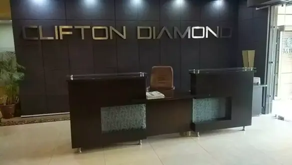 Reception desk at Clifton Diamond in Clifton with black wall signage, modern wooden counter, chair, vase, plant, and glass do
