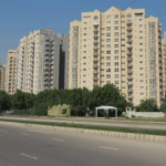 Row Of Modern Beige High-Rise Apartment Buildings Along Wide Boulevard With Palm Trees And Streetlights