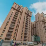 Tall Beige High-Rise Towers Of Lakhani Presidency Apartment Complex With Balconies, Modern Entrance Gate, And Parked Cars