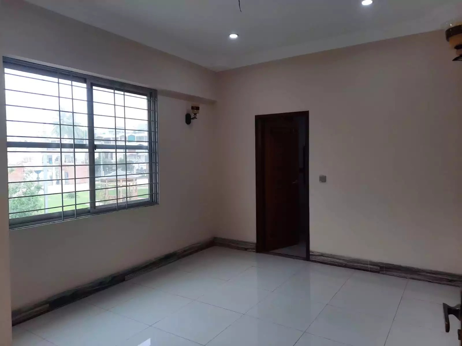 Spacious empty room in Karachi Beach Residency flat, Clifton Block 3, with beige walls, white tiled floor, large grilled wind