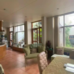 Spacious Open-Plan Kitchen, Dining, And Living Area With Wooden Cabinets, Island Counter, Large Glass Windows, Sofa, Dining T