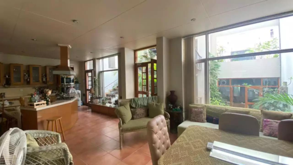 Spacious Open-Plan Kitchen, Dining, And Living Area With Wooden Cabinets, Island Counter, Large Glass Windows, Sofa, Dining T