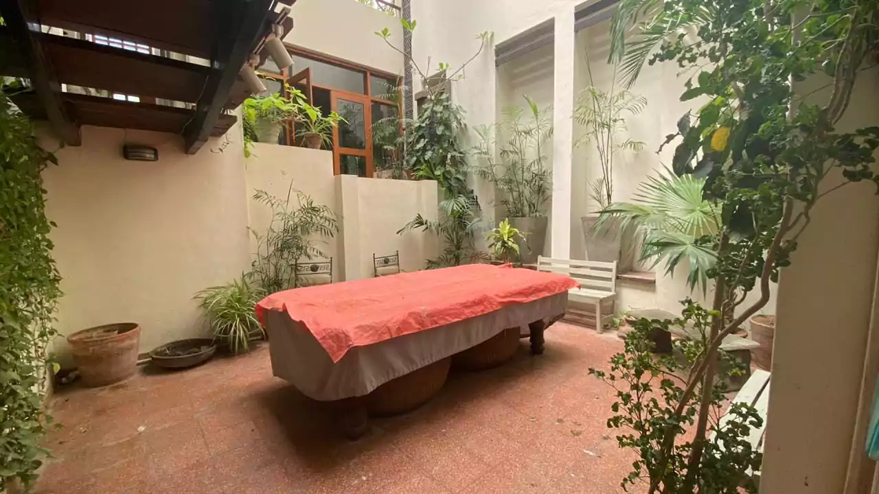 Elegant 500 Square Yards Bungalow for Sale in DHA Phase 6, Karachi (1) Lush courtyard with covered billiard table, tropical plants, wooden shutters, and terracotta pots in DHA Phase 6 bungalow
