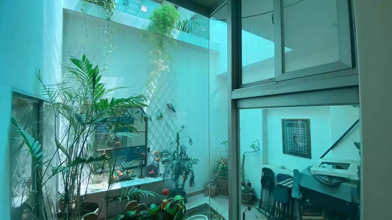 Elegant 500 Square Yards Bungalow for Sale in DHA Phase 6, Karachi (7) Lush indoor atrium with tropical plants, glass walls, fish tanks, seating area and desk in 500 sq yd bungalow, DHA Phase 6